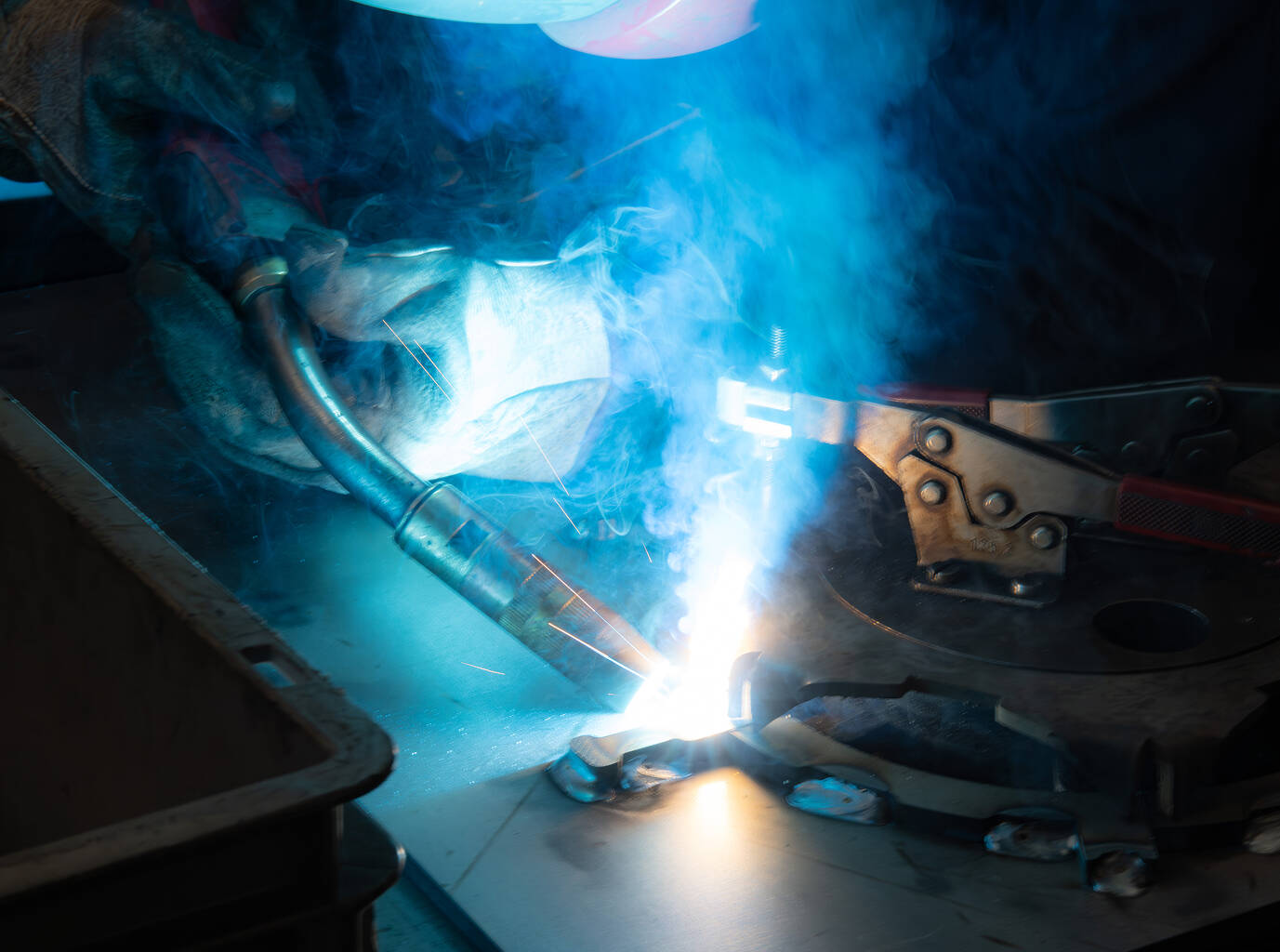 Una persona che salda parti metalliche, producendo una luce blu intensa e fumo