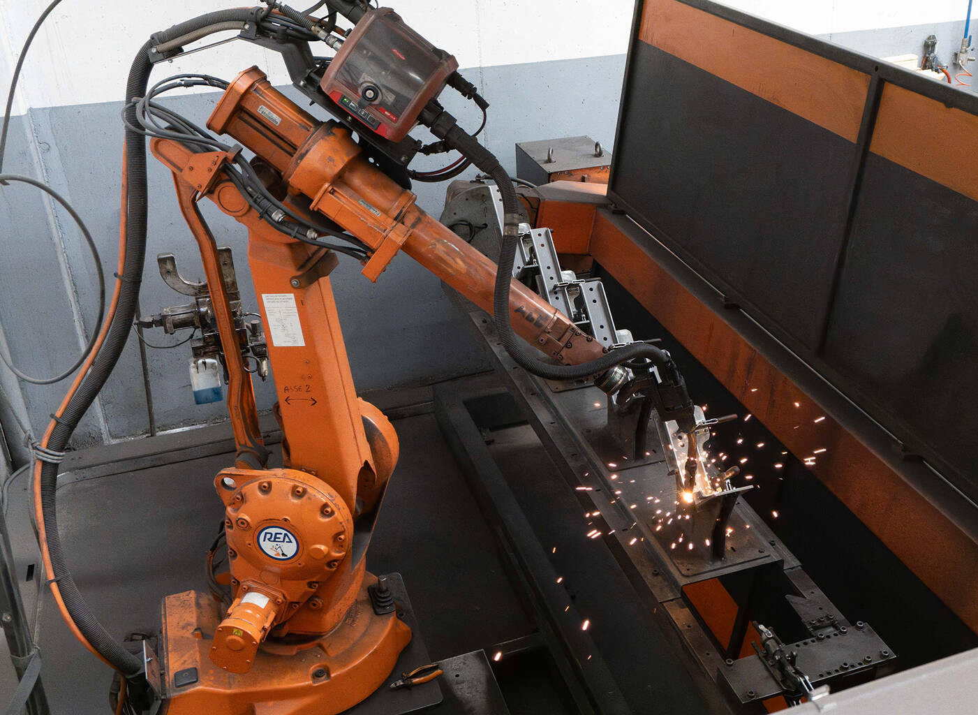 Braccio robotico industriale arancione che salda un componente metallico con scintille