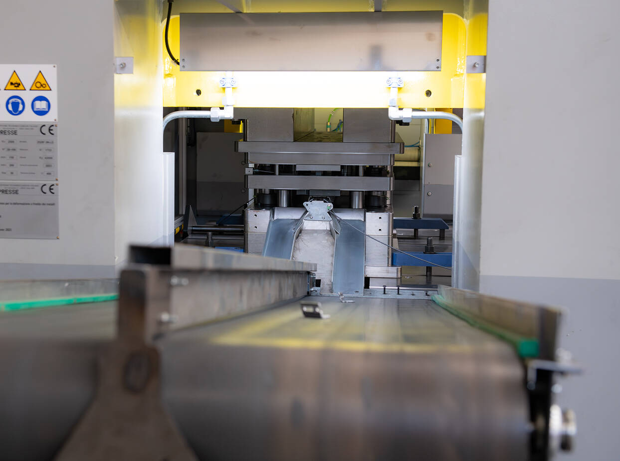 Pressa industriale con nastro trasportatore e segnali di sicurezza in un'officina meccanica