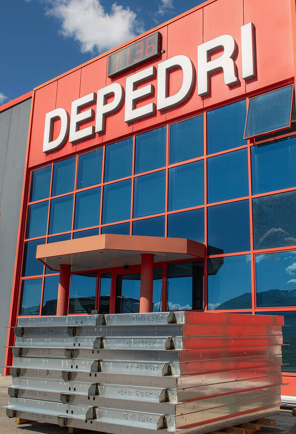 Facciata dell'azienda Depedri con insegna rossa e componenti metallici impilati in primo piano